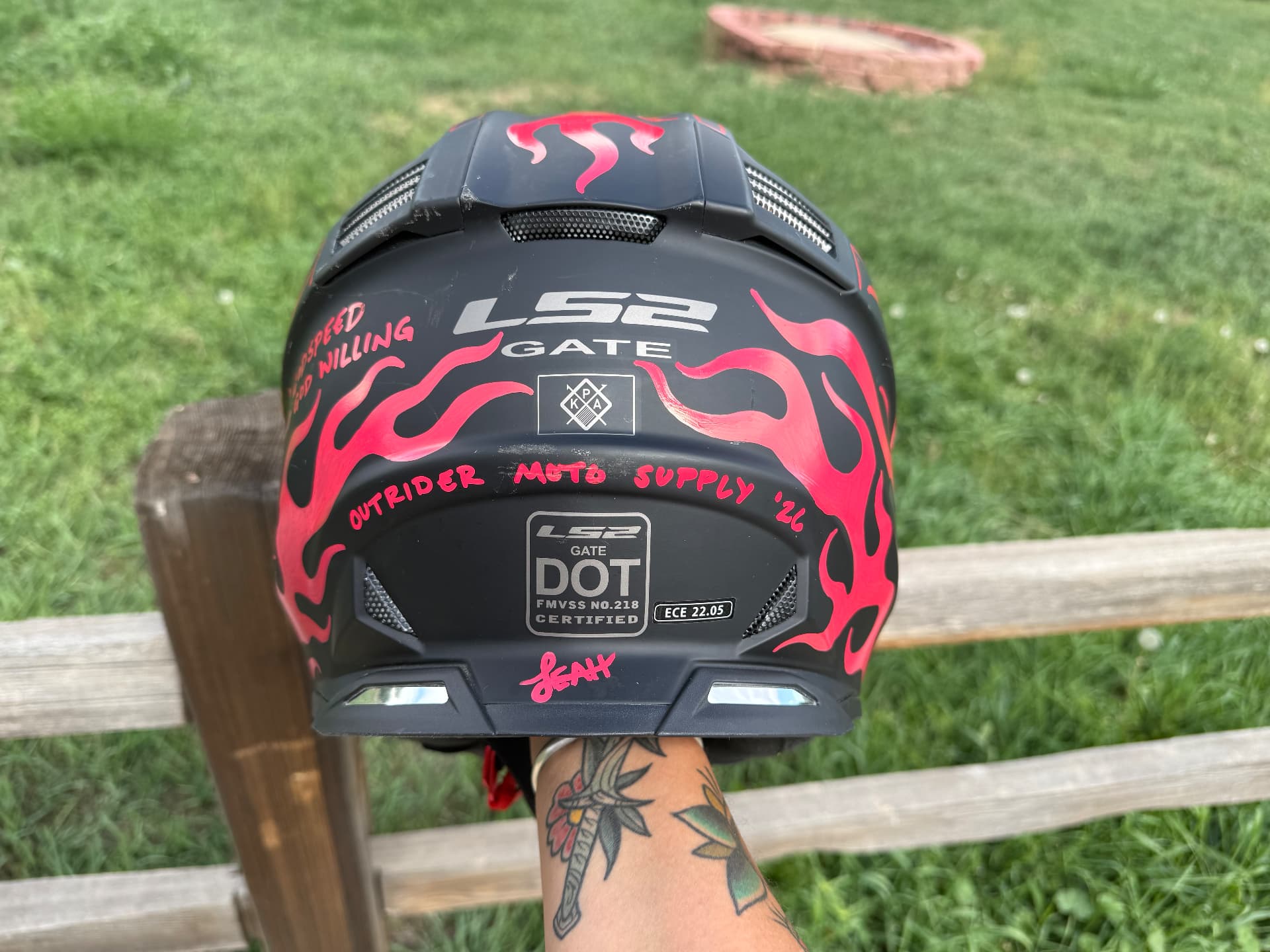 Rear of a black MX helmet signed Outrider Moto Supply in pink paint